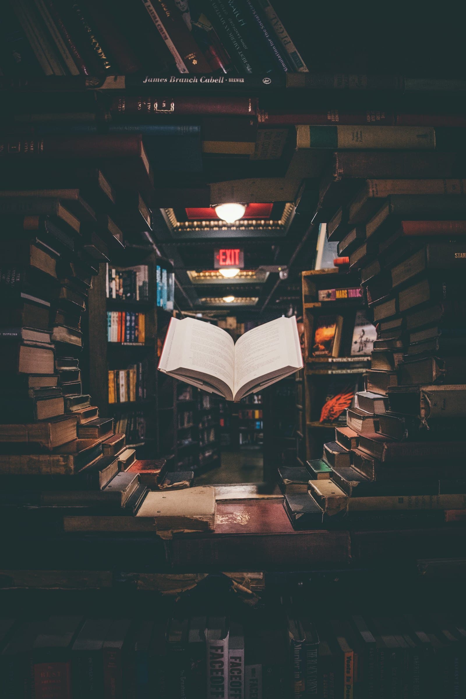 An open book suspended among towering shelves of old books in a dim study.